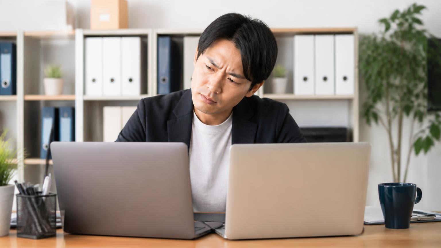 同名の別会社と区別する｜事務所のパソコン前で男性1人が画面を見比べて首をかしげる