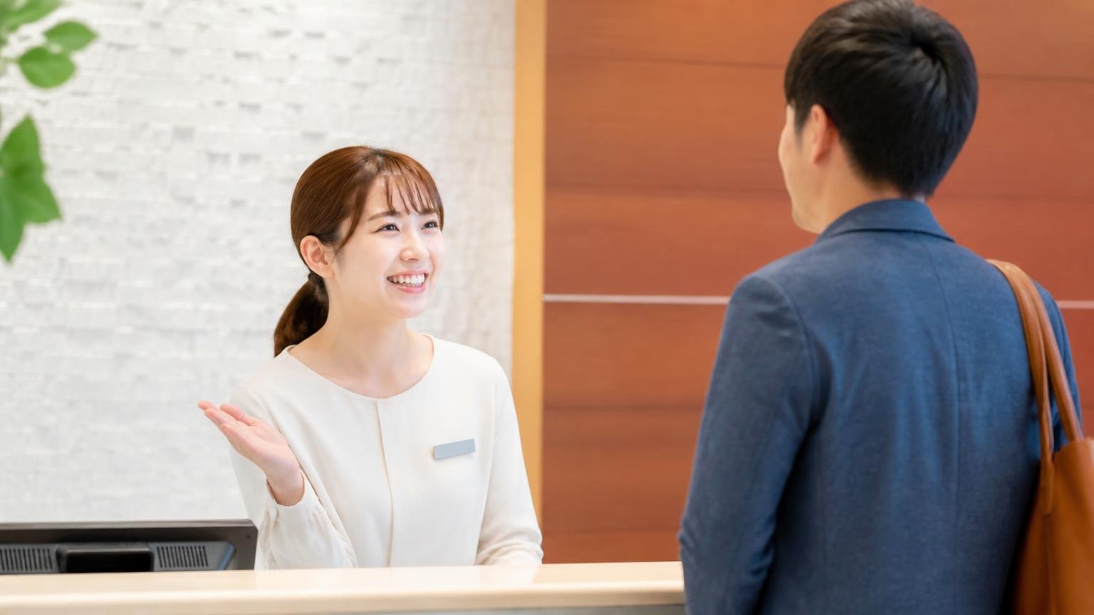 受付スタッフの対応を評価する声 明るい受付カウンターで来客を笑顔で迎える女性1人と男性1人