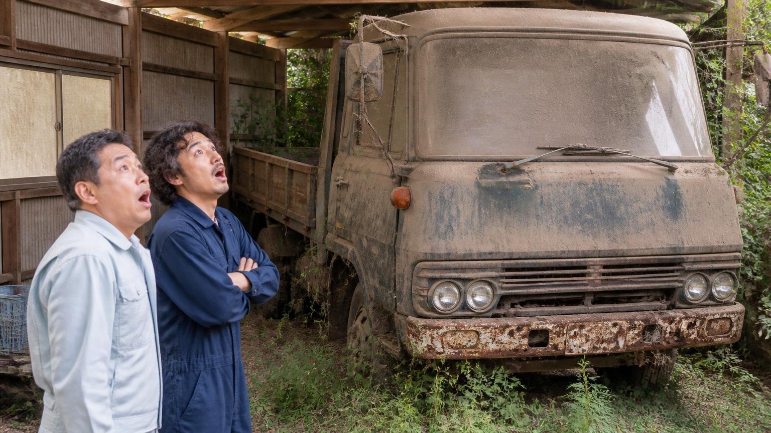 低年式や不動車でも値がついた声 草の生えた車庫の隅で埃をかぶった古いトラックを男性2人が見上げて驚く