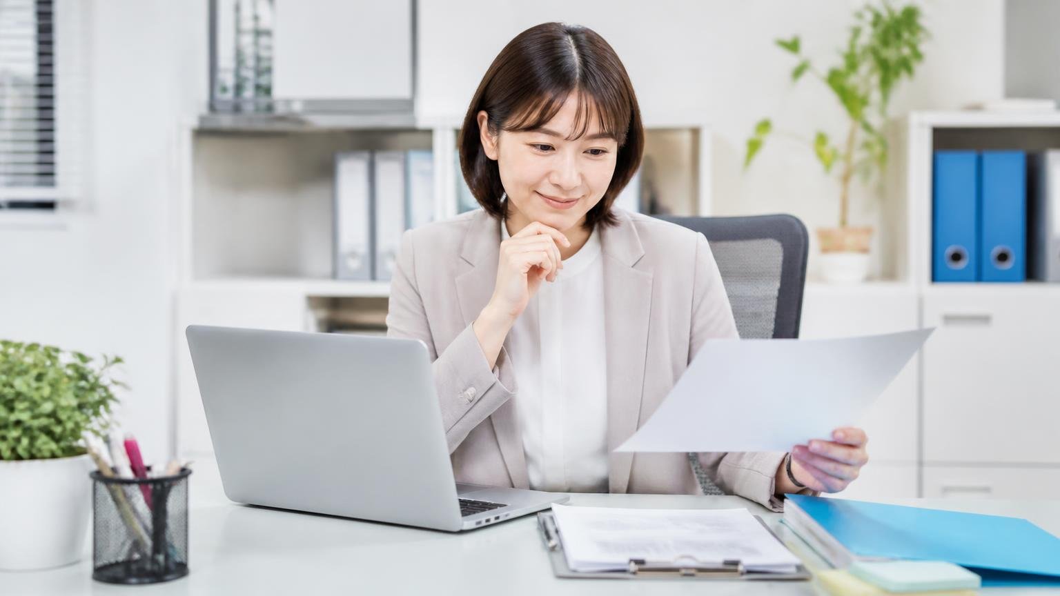 運営会社や設立年や法人番号を照らし合わせる。事務所でパソコンと書類を見比べる女性1人が納得の表情