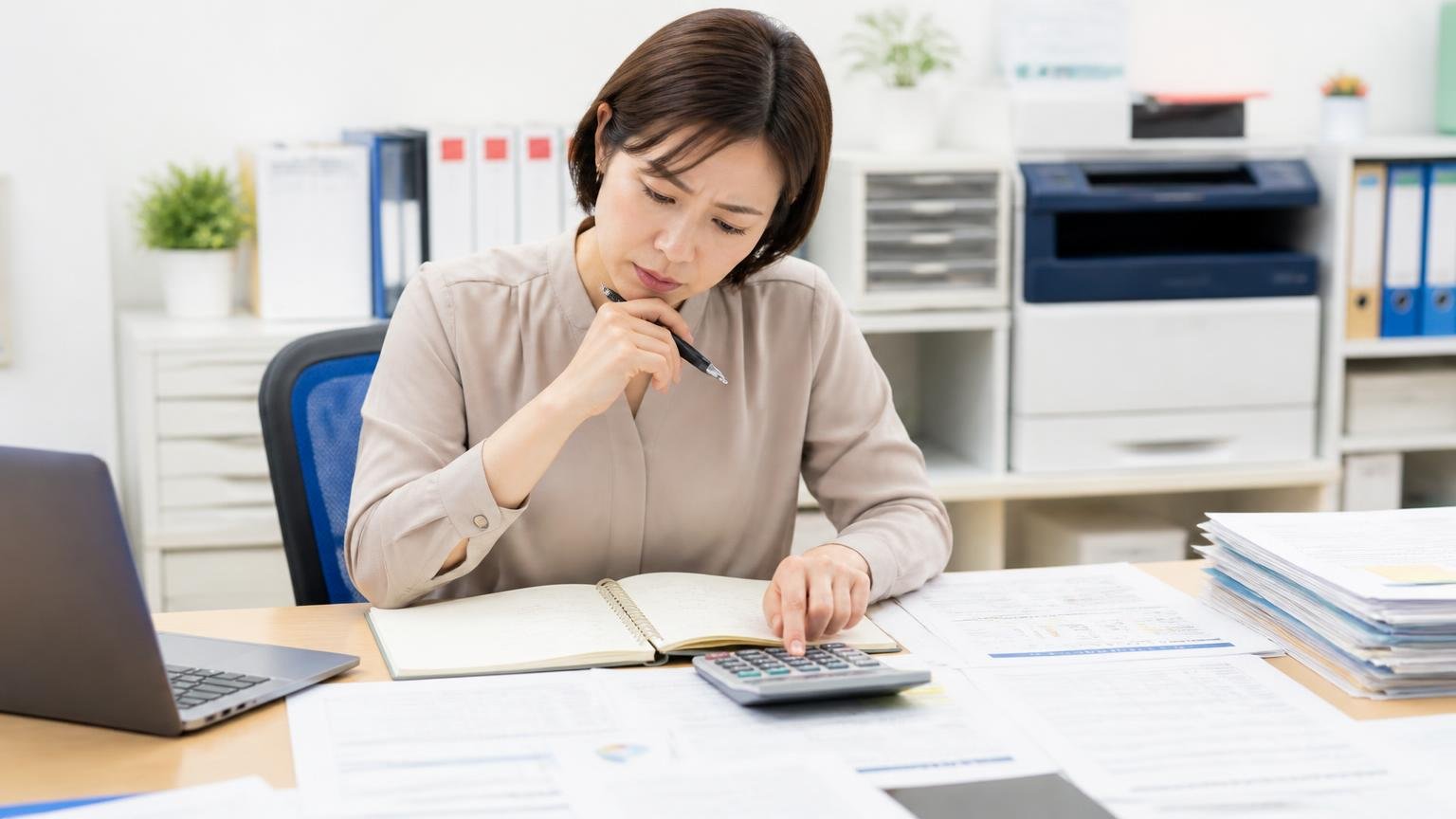 詰まる前提で予算を組むという考え方 事務所の机で電卓を叩いて年間の維持費を計算する 女性1人 メモを取りながら考え込む