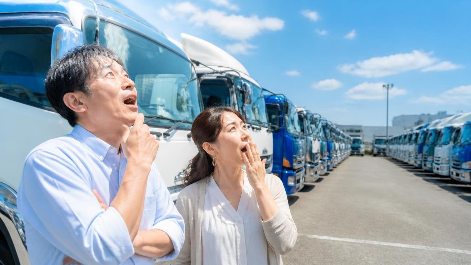展示場の広さ・在庫の多さを評価する声。広い屋外展示場に並ぶ中古トラックを見上げて驚く男性1人と女性1人