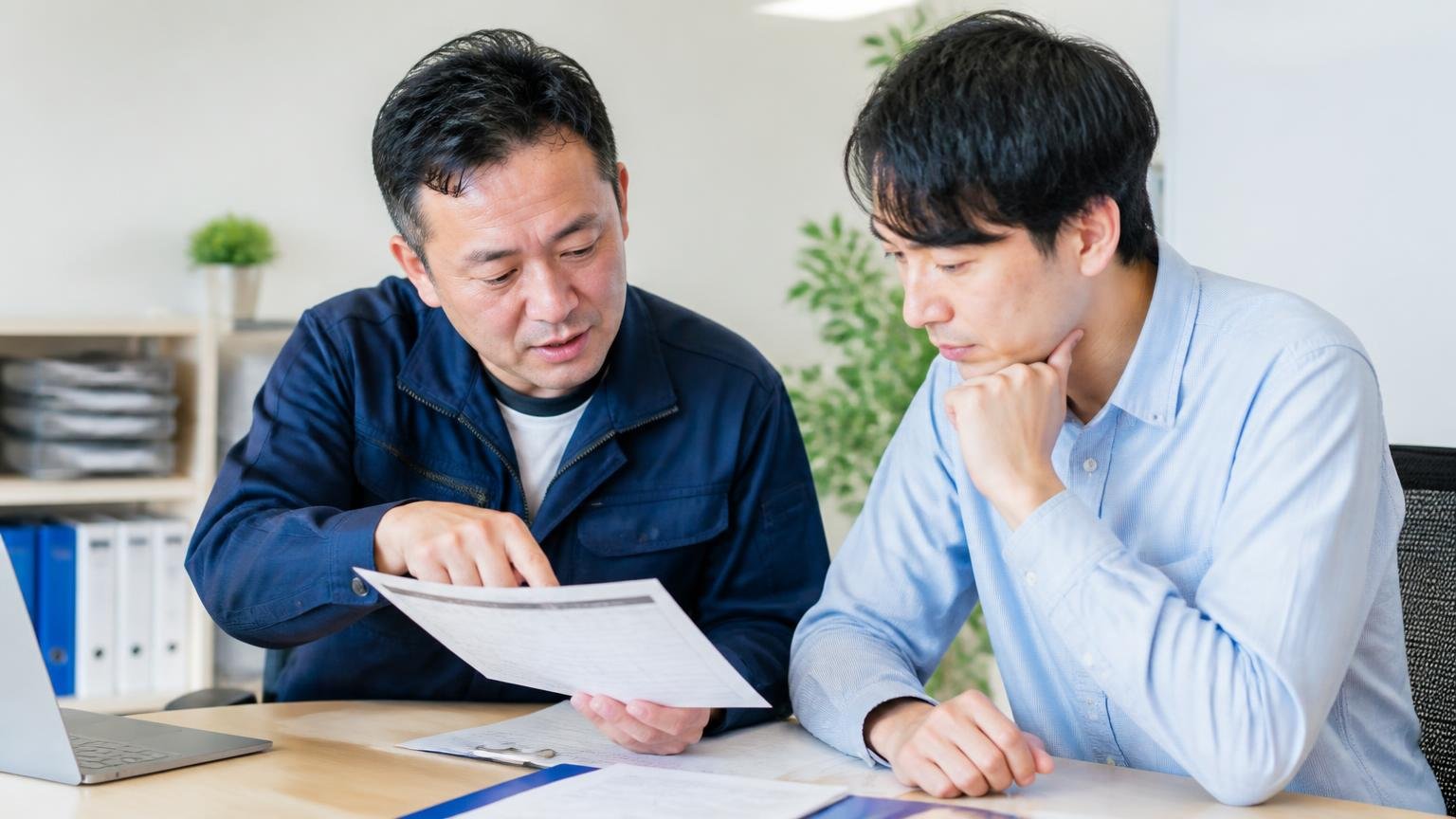 どんな場合にいくら減額されるのかを書面でもらう。事務所で査定書を見ながら打ち合わせする男性2人、指さして確認する