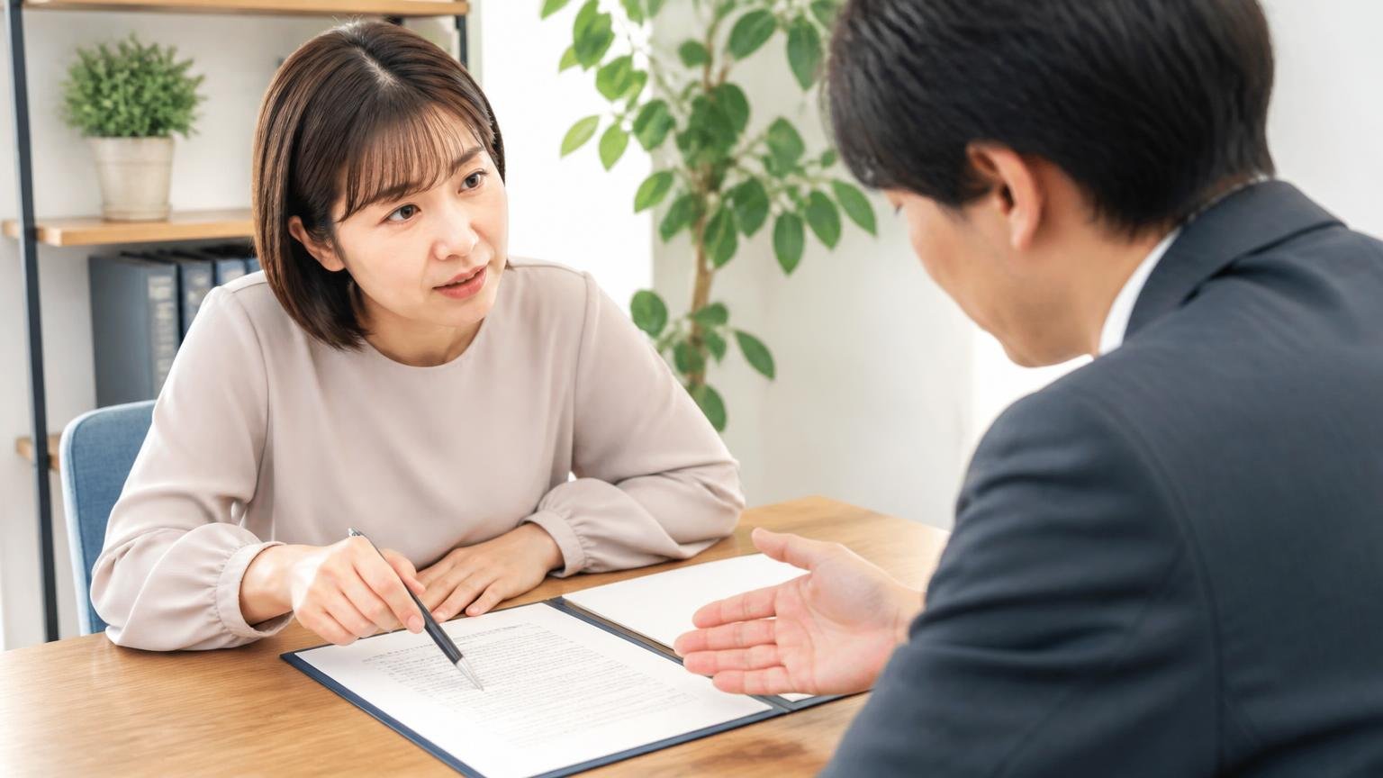 書面で条件を確認する場面。事務所で契約書の条件欄をペンで指しながら質問する女性1人と答える担当者1人