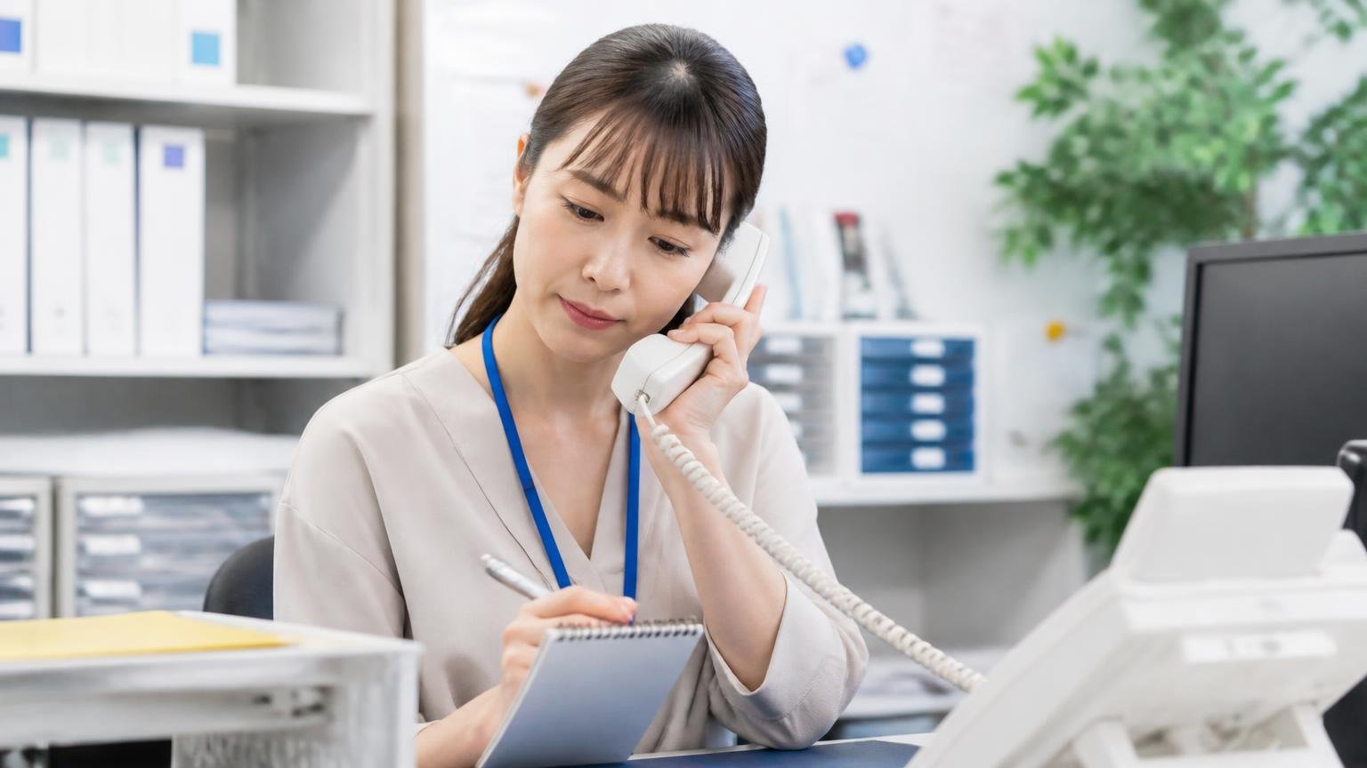 電話の概算を目安として受け取る 事務所の電話の前でメモを取る女性1人が真剣な顔でうなずく
