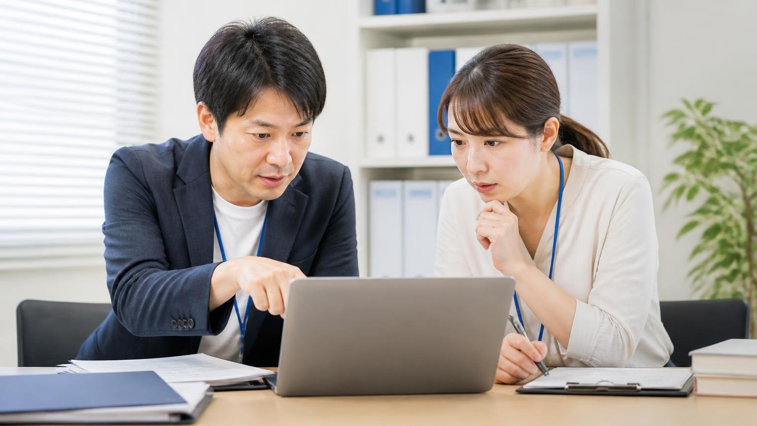 会社概要と古物商許可と拠点の確認、事務所でパソコンの会社概要ページを指さしながら男女2人が真剣に確認する場面