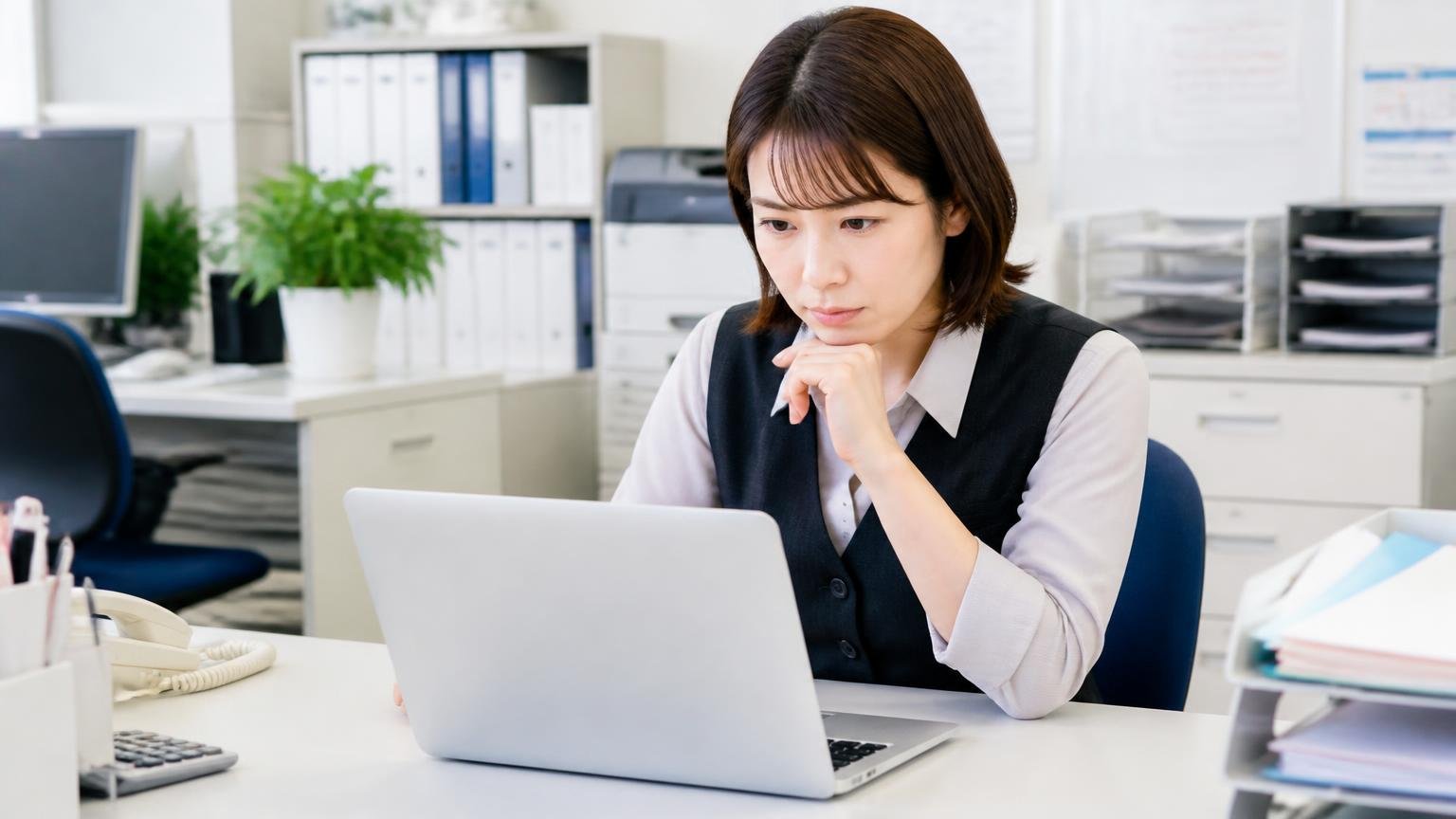 会社概要|1980年創立、旧社名は「自興中販」。事務所の机で女性事務員1人がパソコンの会社案内を真剣な顔で確かめる
