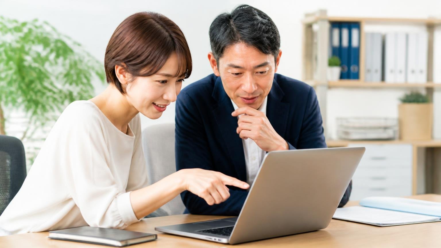 運営は有限会社パークノール商会|会社概要と所在地 事務所でパソコンの会社概要ページを指さし確認する30代女性と40代男性