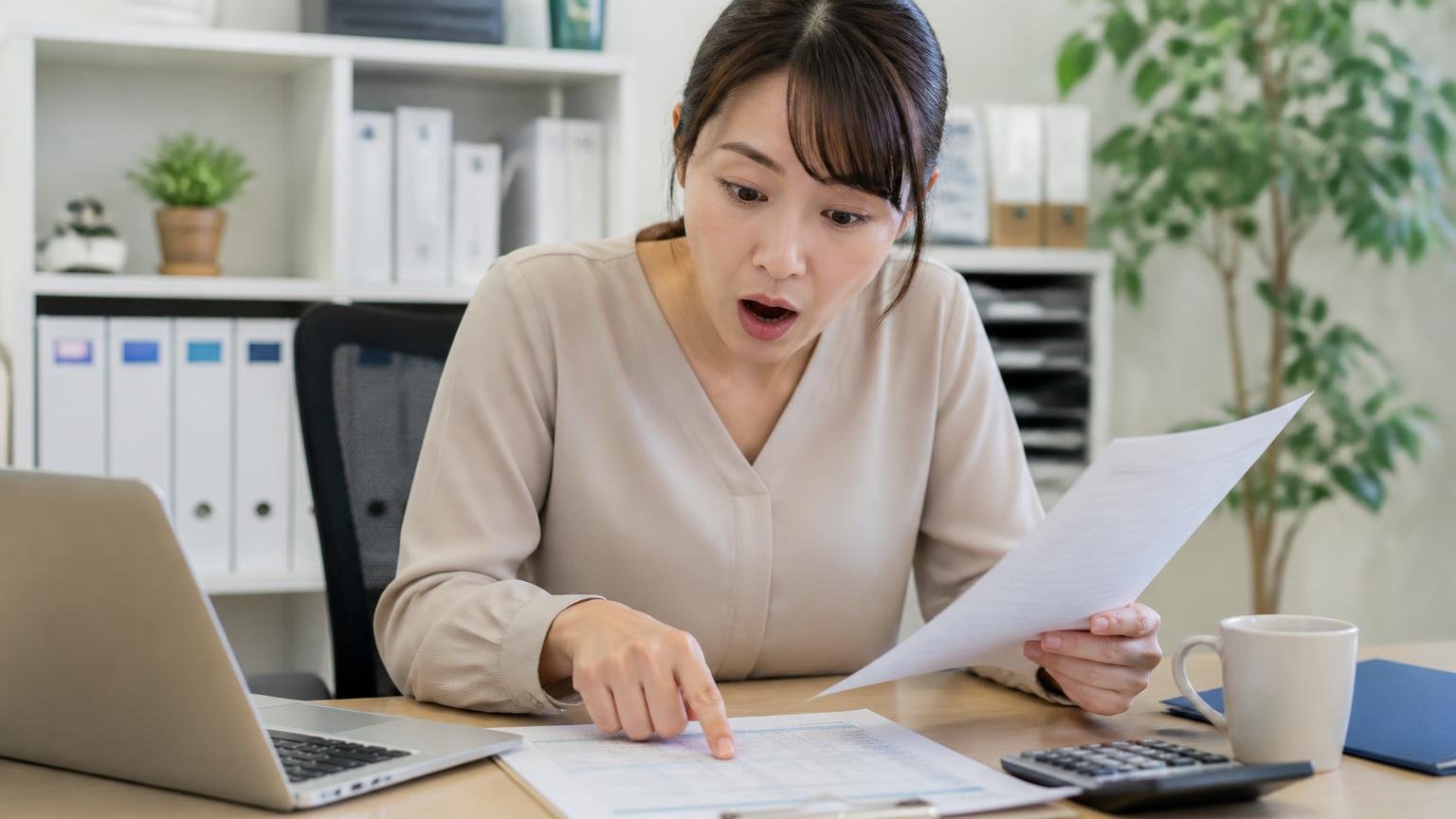 公式サイトに無料と書かれている範囲の確認、事務所の机で見積書の項目を指でなぞりながら女性1人が驚いた表情を見せる