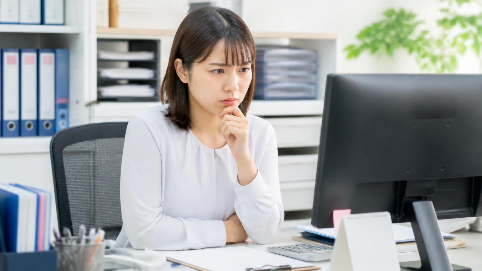 公式サイトが書いている買取の方針と書かれていない条件、事務所のパソコンで公式サイトの買取ページを見て考え込む女性事務員1人