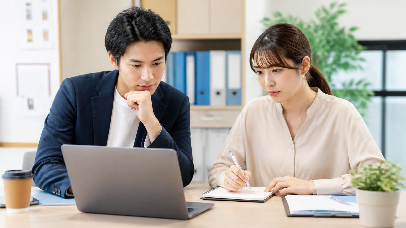 公式サイトに書かれている買取条件と、査定前に確認したい点(事務所の机でノートパソコンを見ながらメモを取る男女2人が真剣にうなずく)