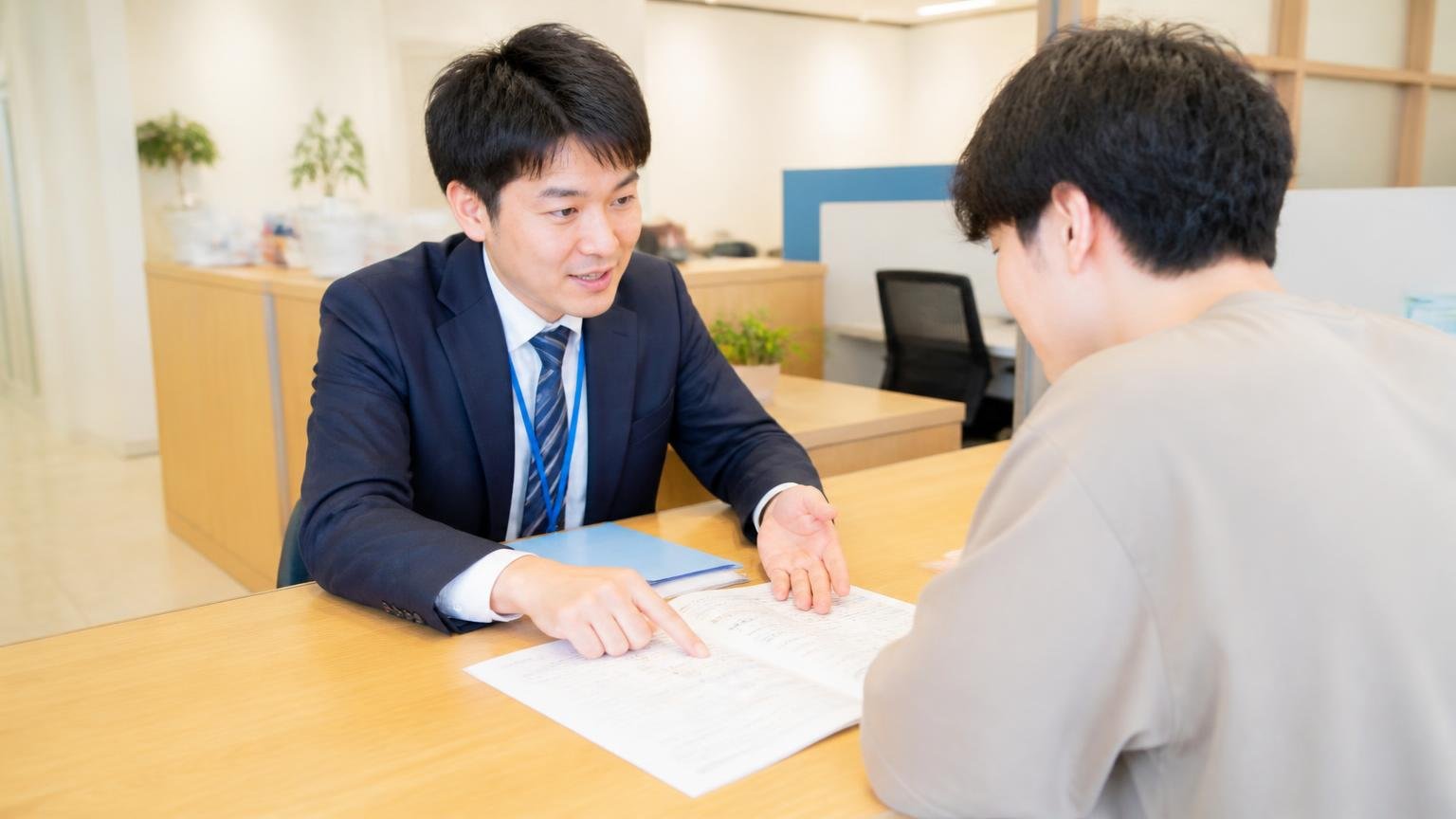 わからないことは細かく教えてくださりという口コミ。事務所のカウンターで書類を広げ若い客に丁寧に説明する担当者