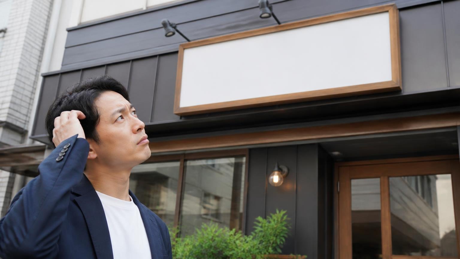 あなたが連絡する「その店舗」を運営しているのは誰か 店舗の看板を見上げる男性1人が首をかしげる表情