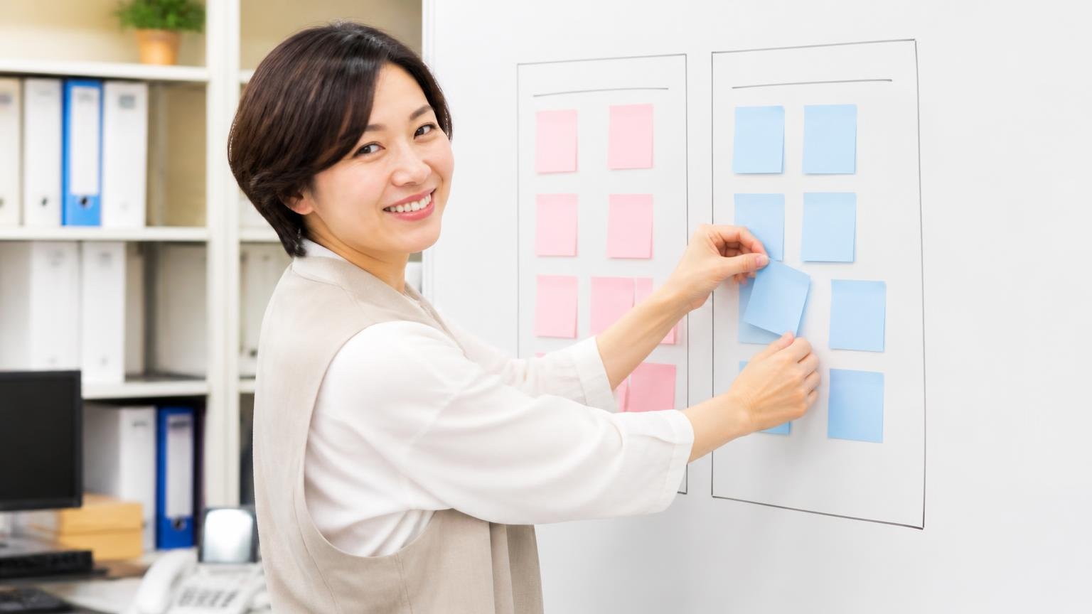 悪い口コミは「金額」と「対応」に分けて読む 事務所のホワイトボードに2つの枠を書いて付せんを仕分ける女性事務員1人、納得の笑顔