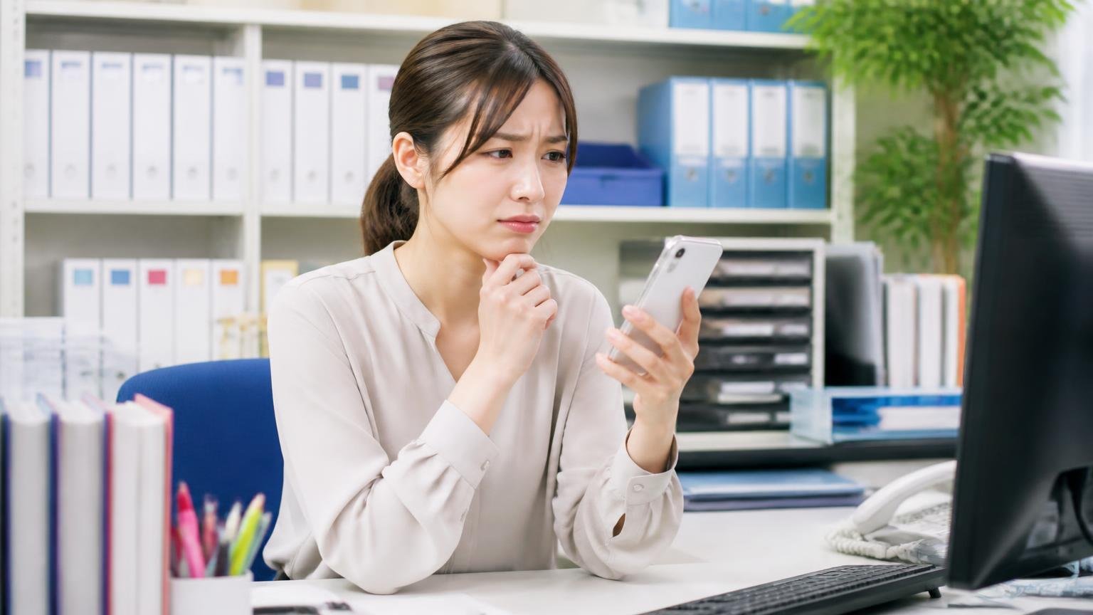 公式サイトに書かれていないこと｜対応エリア・書類代行・減額条件・現金化の期日｜事務所でスマホを片手に公式サイトを見ながら首をかしげる女性事務員1人