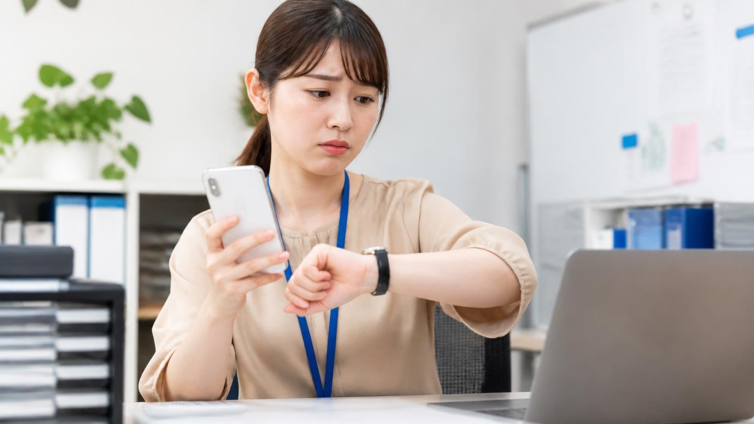 同じ問い合わせで返事が来た人と来なかった人がいる 事務所でスマホの着信履歴を確認して待っている場面 女性1人 時計を気にする表情