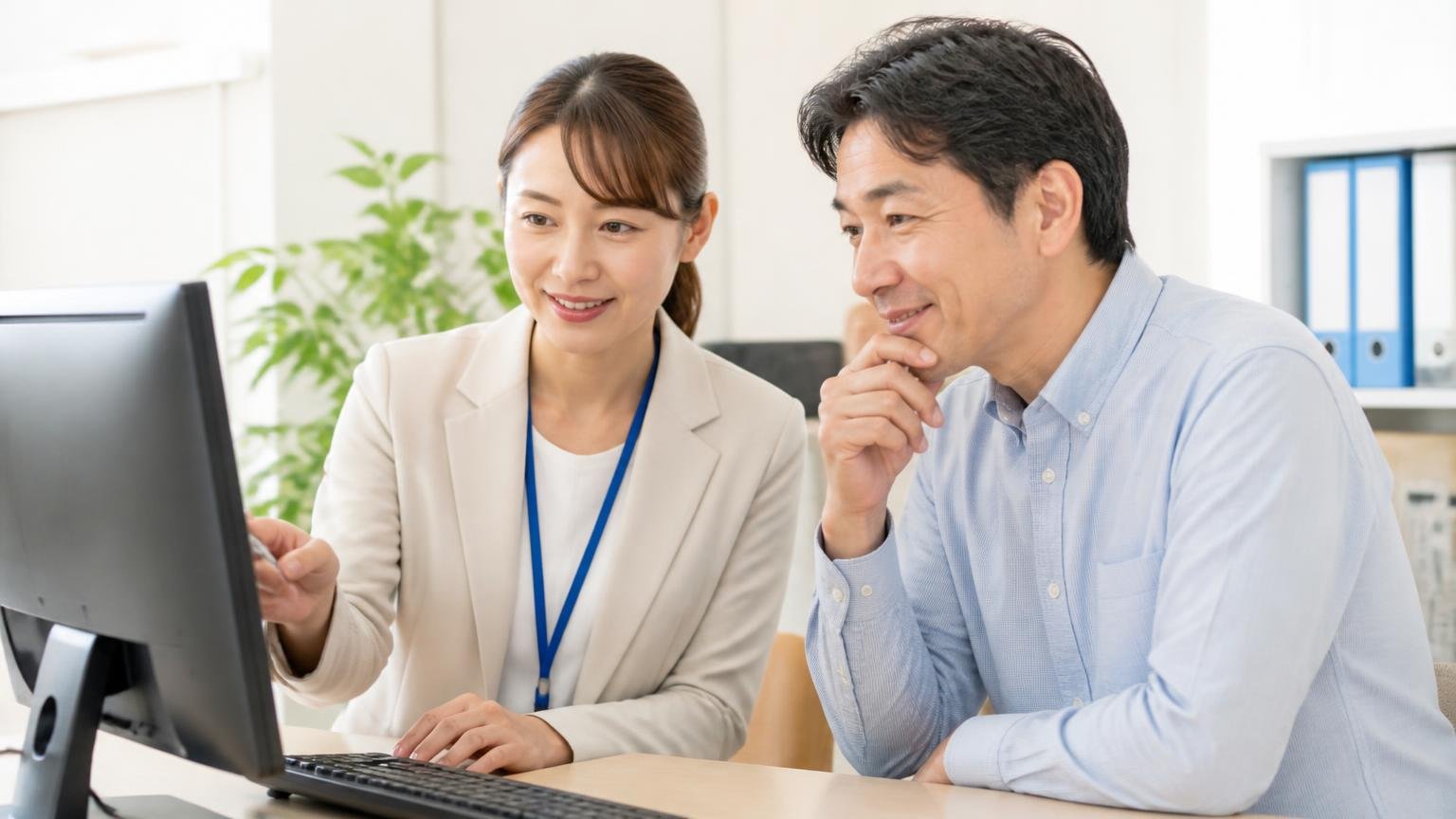 公式サイトに書かれた買取条件:査定も出張査定も無料、事務所でパソコン画面を確認する場面、事務員の女性と夫の2人、うなずいて安心する