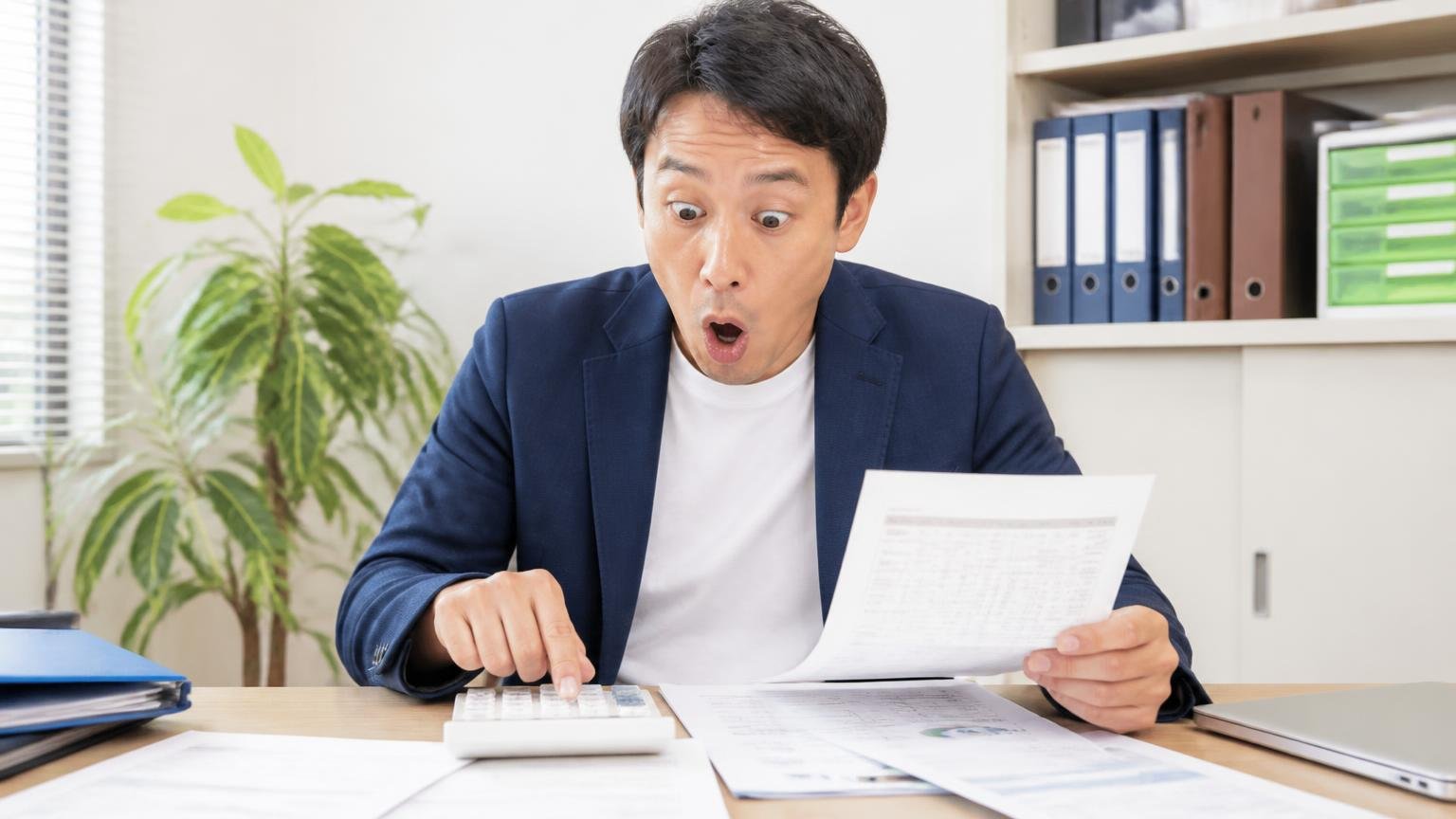 自動車税・自賠責・リサイクル料金は「売却」と「廃車」で扱いが違う 事務所で電卓と書類を広げた40代男性が計算して目を丸くする