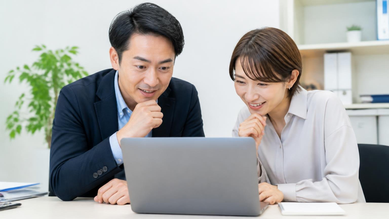 古物商許可番号と会社情報を公式サイトで確かめる 事務所でパソコンの会社概要ページを見る男女2人がうなずきながら確認する