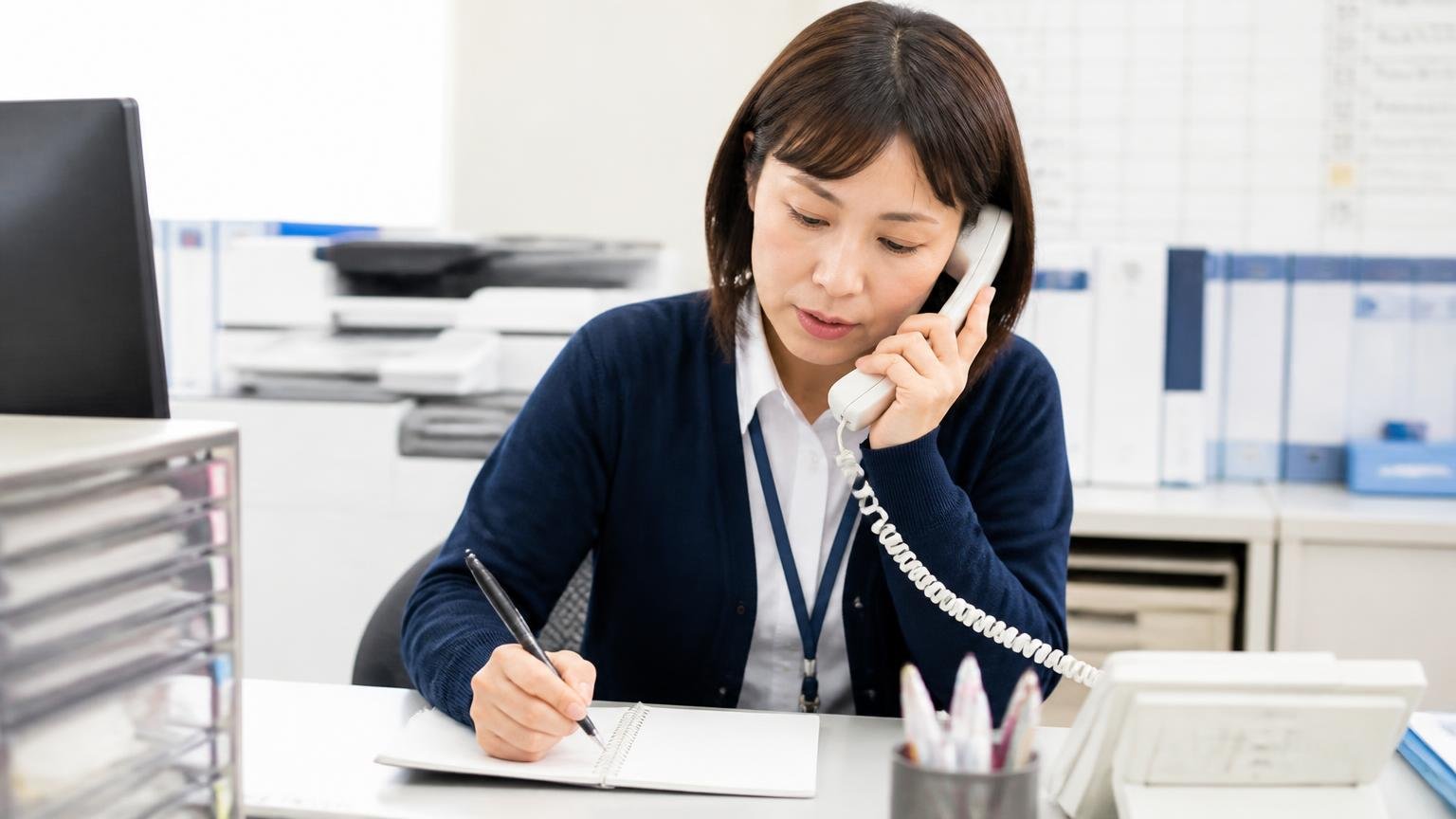 電話で最初に聞く5つのこと 営業所の事務机でメモを取りながら電話する女性1人、真剣な表情
