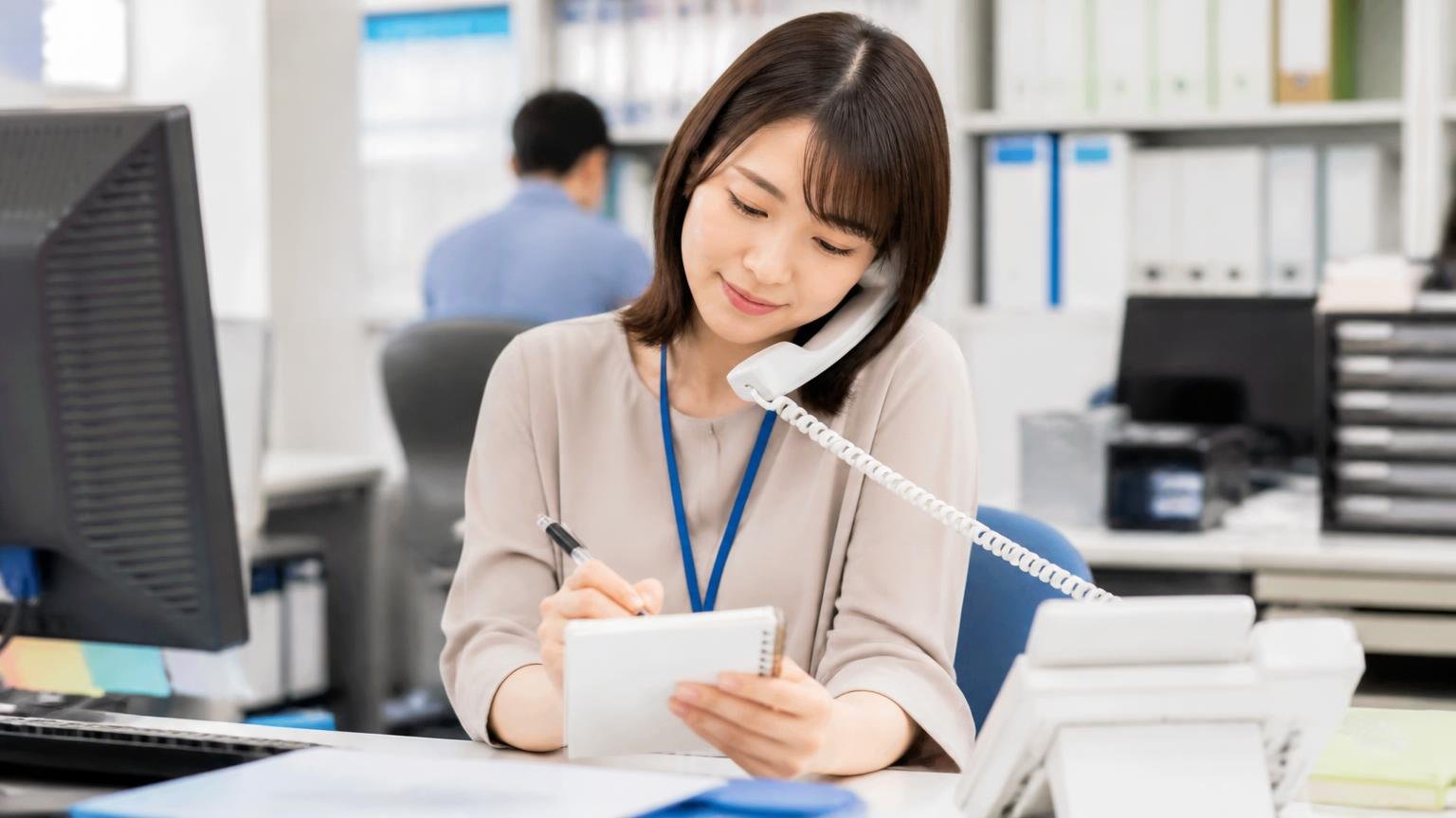 問い合わせで最初に聞いておきたい5つのこと 事務所でメモ帳を片手に電話をかける女性1人が、うなずきながら書き込んでいる