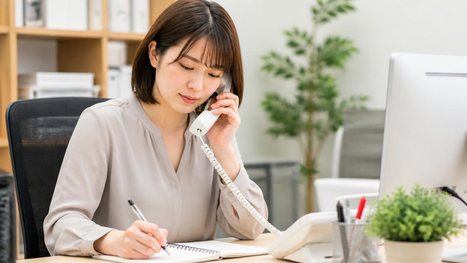 手順①｜電話では「何社か見てから決めます」だけ伝え、希望額は言わない｜事務所で電話をかけながらメモを取る女性事務員1人が落ち着いた表情