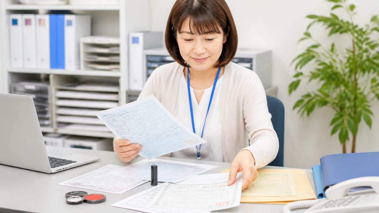 査定の前にそろえておきたい書類と準備 事務所の机で車検証や印鑑証明書をそろえる女性事務員が安心した表情