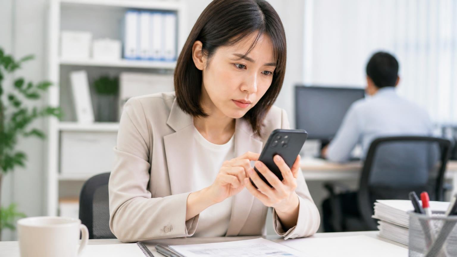 調べる相手を切り替える場面。事務所の机でスマホに1社の社名を打ち込む女性1人が真剣なまなざし