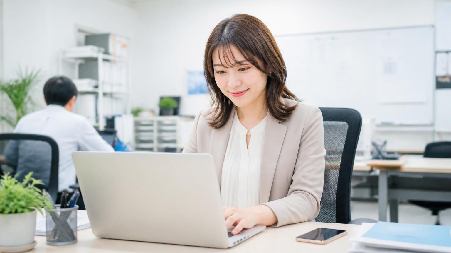 電話が苦手ならメールのみを最初に指定できる。事務所でスマホを置いてパソコンでメールを打つ30代女性がホッとした表情の場面