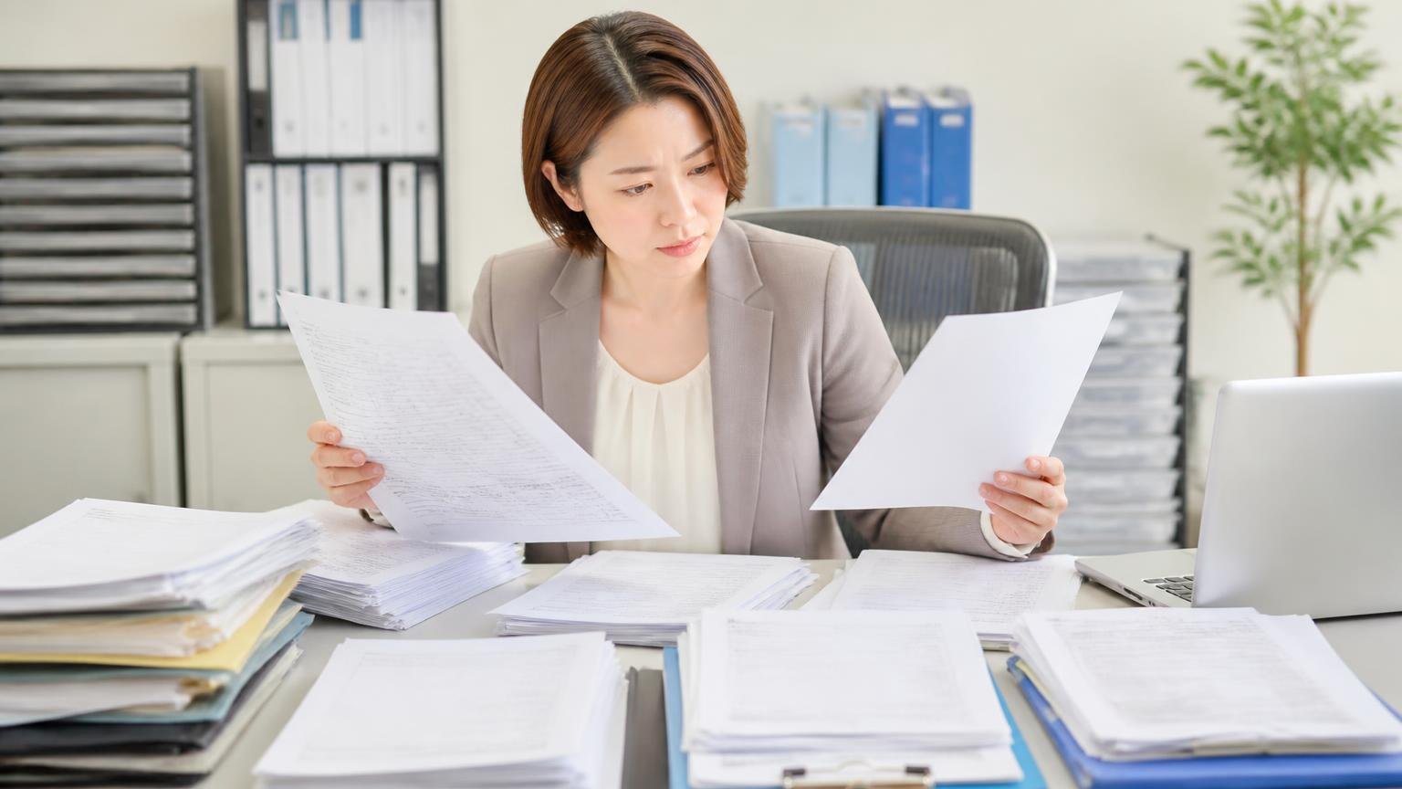 必要書類は抹消済みか法人所有かで変わる、事務所で女性が書類の束を広げて確認する場面