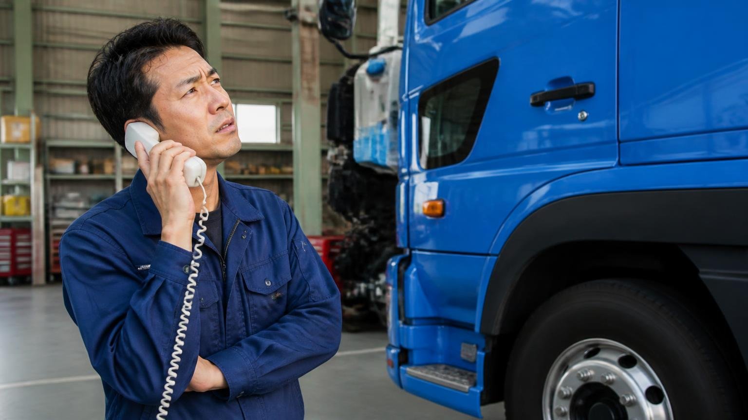 概算は現車を見ていない数字である／車庫で電話をしながらトラックを見上げる男性1人／受話器を持ったまま眉を寄せる