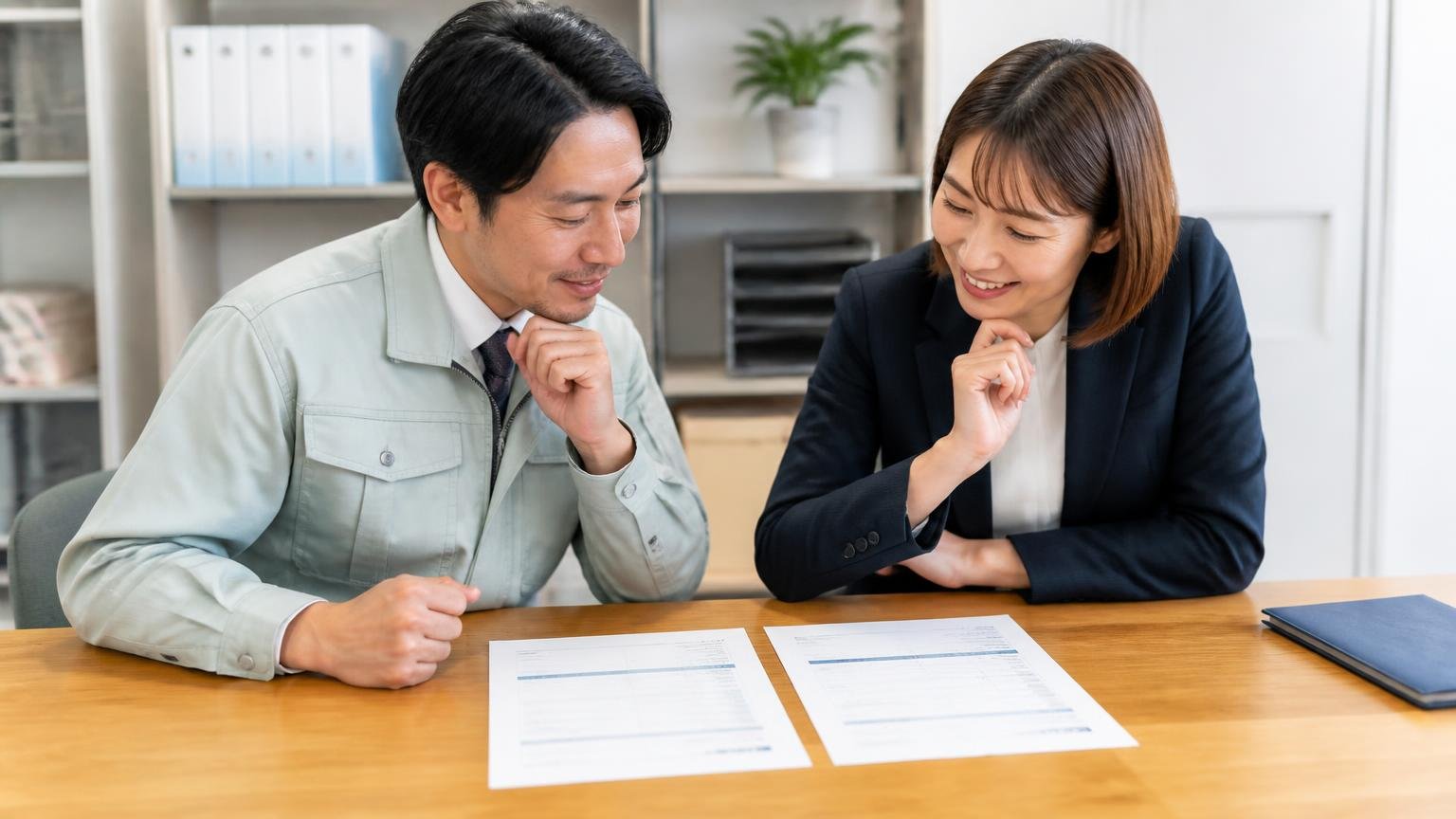 越村商店の見積書の隣に置く1社を選ぶ 事務所の机に2枚の見積書を横に並べて見比べる男性1人と女性1人が納得の表情