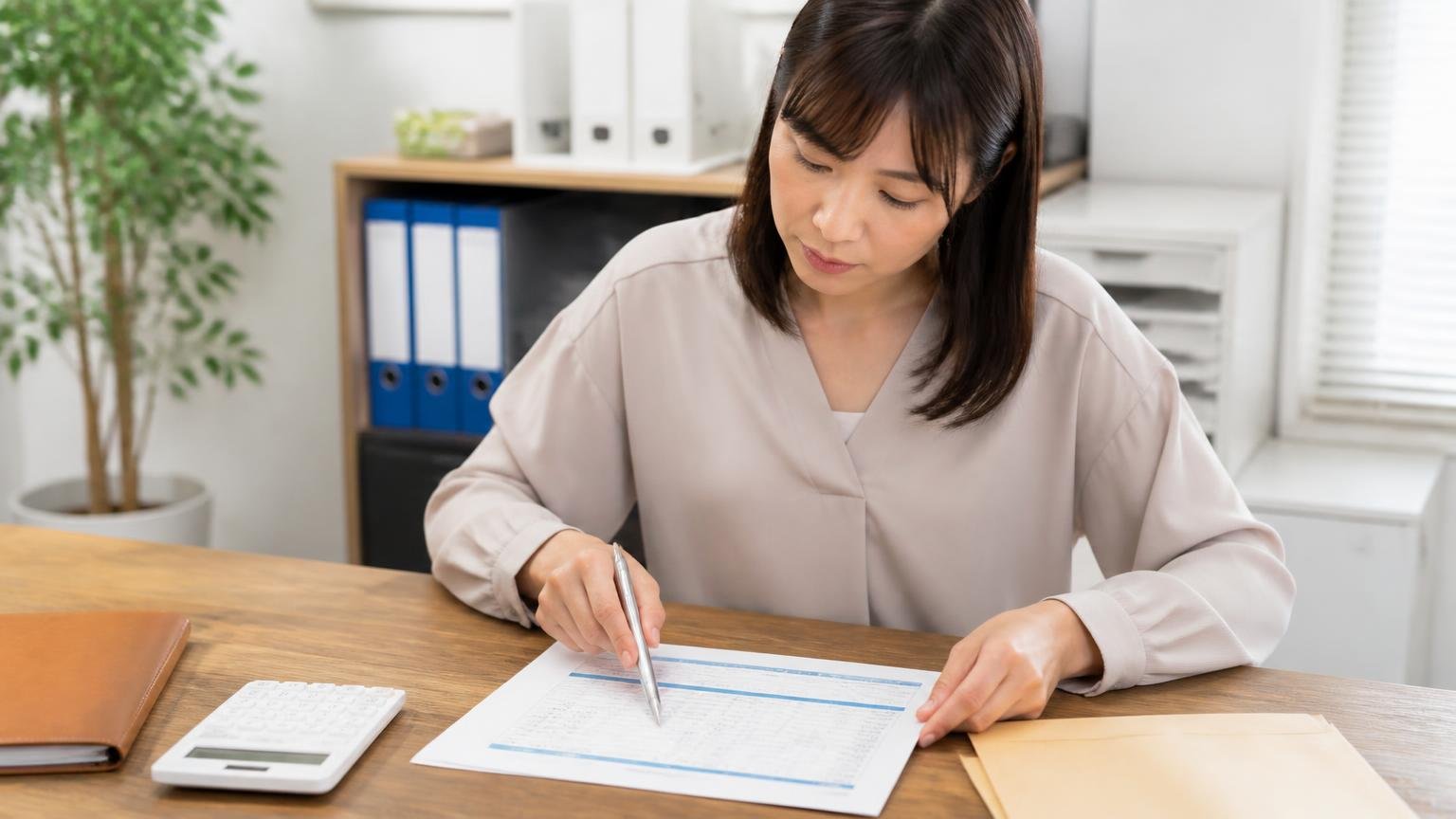 見積書の金額は車両の値段だけではない。事務所の机で女性が見積書の内訳をペン先でなぞって確認する