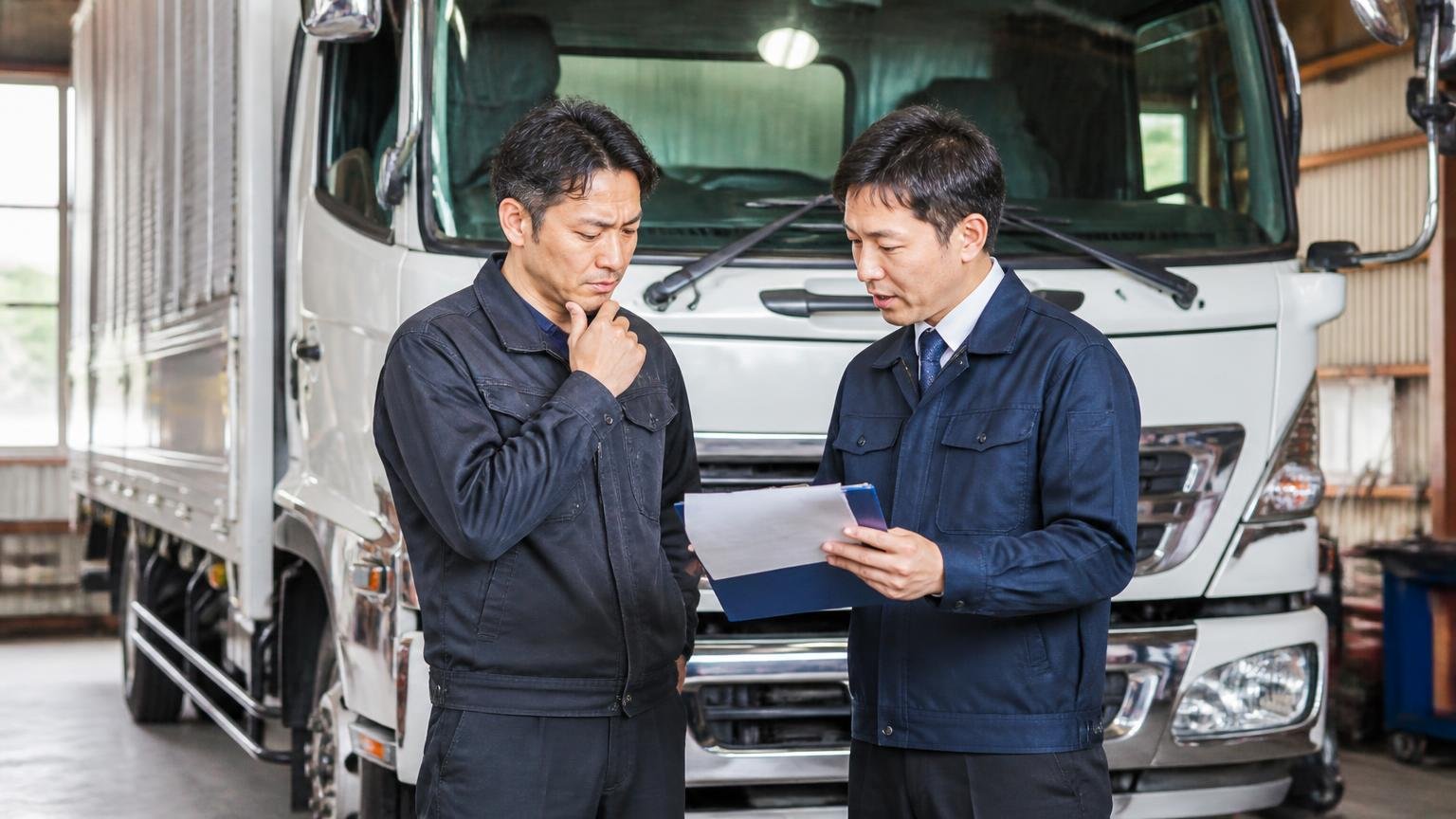 仮金額と最終金額は別物 車庫で実車査定を受けるトラックの前 男性2人 書面を見て話す