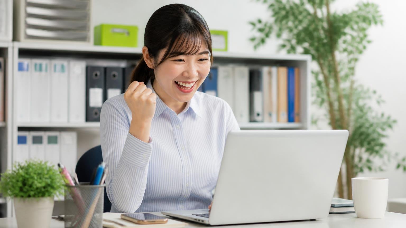 地元業者の金額と比べる、事務所でノートパソコンからトラックの無料査定を申し込み笑顔でガッツポーズする女性事務員