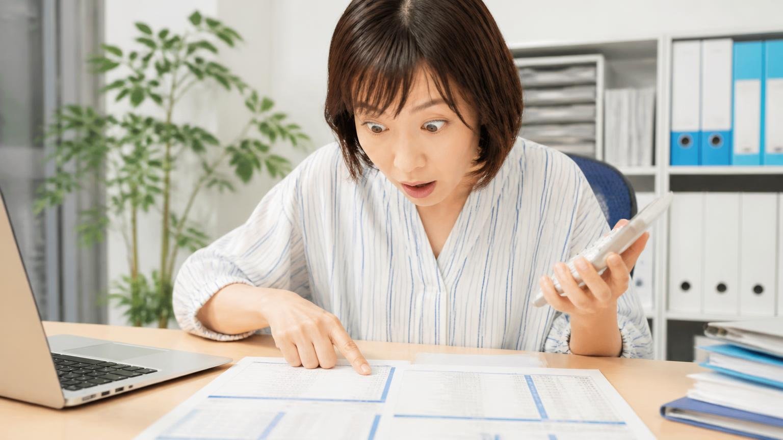 査定料・出張費・書類手続きの無料の範囲が書いてあるか 事務所の机で見積書を広げる場面 女性1人が電卓を片手に項目を指でなぞり目を見開く
