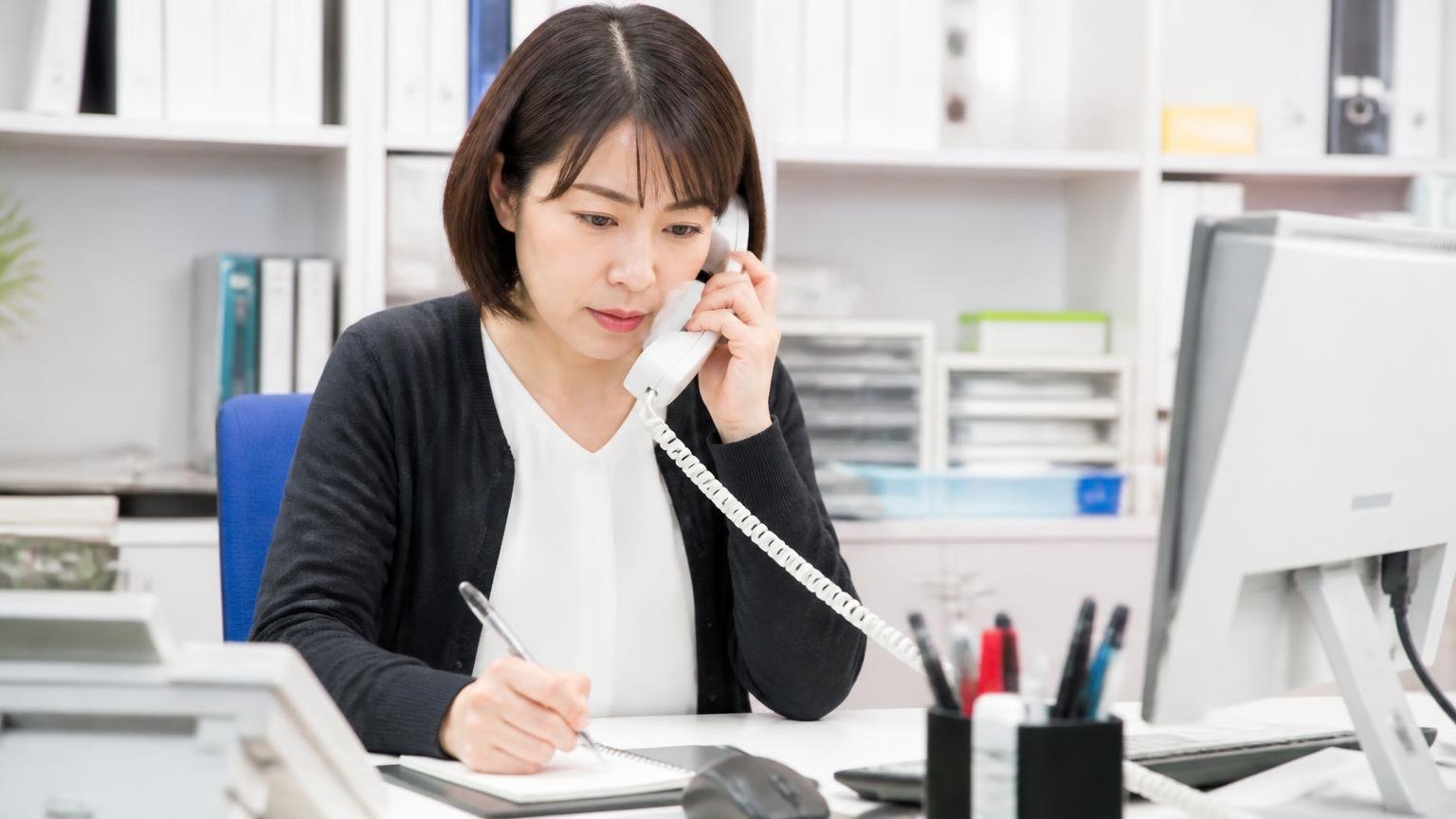 電話やネットの概算は下がる条件とセットで聞く 事務所で女性事務員1人が受話器を持ちメモを取りながら真剣な表情